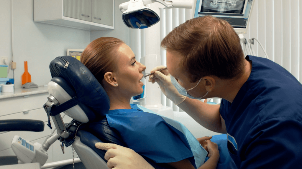 a man in a blue uniform and gloves holding a woman's mouth. Dentist examining a patient’s mouth during a wisdom teeth evaluation